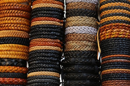 Photo closeup of many different male and female braided leather belts different colors fashion accessory stacked on display for sale outdoor on white background, horizontal pictureの写真素材