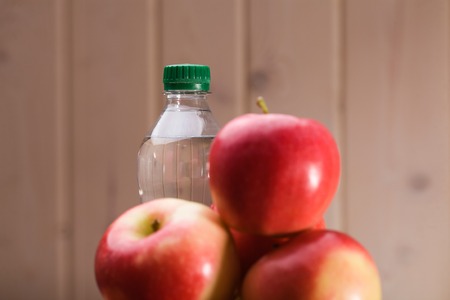 Bunch of bright ripe sweet pure red yellow apples with sealed bottle of water on beige wall background, horizontal photoの写真素材