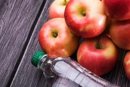 One plastic bottle of soda lies near group of big juicy raw red yellow apples on grey wooden table, horizontal photoの写真素材