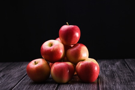 Group of appetizing raw red yellow apples with smooth peel in pyramid shape on wooden table on black background, horizontal photoの写真素材