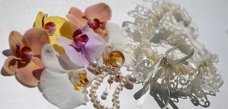Beautiful adorable bridal wedding accessories pearl bracelet earrings golden rings lacy retro garter decorated with petals of yellow pink orchids on white background closeup panorama image, horizontalの写真素材