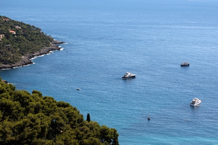 Photo long shot of picturesque resort town hideaway among evergreen trees on mountain slope sailing boats vessels offshore  blue sea on beautiful seascape background, horizontal pictureの写真素材