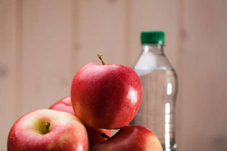 Heap of big sweet fresh red yellow apples and full bottle of water on beige wall background, horizontal photoの写真素材