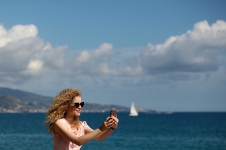 Woman young beautiful with blond long curly hair taking selfie self-portrait photograph on smart...