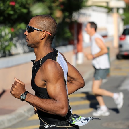 Menton, Roquebrune Cap Martin, France - September 20, 2015: runner half face in sunglasses competes in duathlon running cross city on paved roads on streetscape background, square pictureのeditorial素材