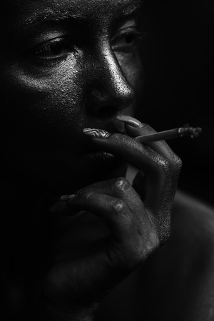 Portrait of breautiful sensual female face painted with silver of young sexual thoughtufl woman smoking cigarette indoor in studio black and white, vertical pictureの写真素材