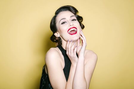 Portrait of attractive sensual glamour retro elegant young adult smiling woman with classic hairstyle and red lips in evening dress indoor on yellow background, horizontal pictureの写真素材