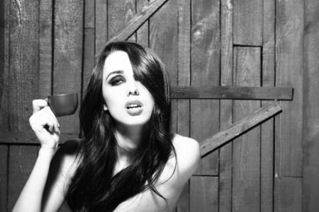 Sensual attractive topless woman with long brunette hair and bright makeup sitting having breakfast of coffee and big burger on wooden background, horizontal pictureの写真素材