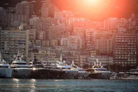 Monte Carlo, Monaco - September 20, 2015: yachts and sailboats modern vessels at moorage in sea port on sun set light shot against mountains on cityscape background, horizontal pictureのeditorial素材