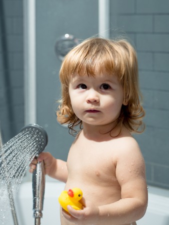 Cute happy smiling funny undressed boy child with blonde curly wet hair taking shower in bath with...