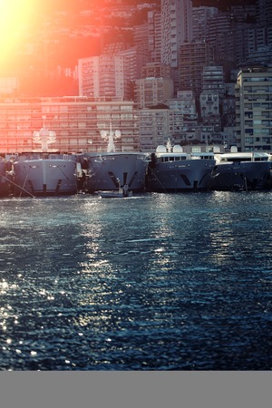 Monte Carlo, Monaco - September 20, 2015: yachts and sailboats modern vessels at moorage in sea port on sunny summer day light shot against mountains on cityscape background, vertical pictureのeditorial素材