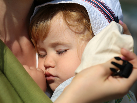 Closeup of cute beautiful carefree innocent baby boy deep sleeping on hands of mother sunny day outdoor, horizontal pictureの写真素材