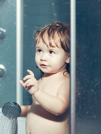 Cute happy smiling funny undressed boy child with blonde curly wet hair taking shower in bath with...