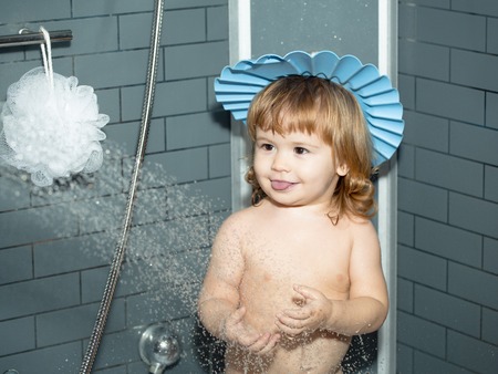 Cute happy smiling funny undressed boy child in blue hat with blonde hair taking shower in bathの写真素材