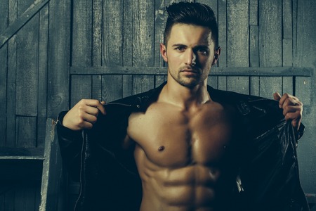 Handsome sexy sensual muscular stylish young man in leather jacket with bare torso standing indoorの写真素材
