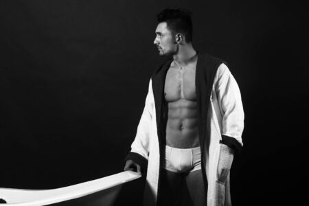 Handsome sensual sexy young man in white panties and terry bathrobe with bare muscular torso and beautiful bodyの写真素材