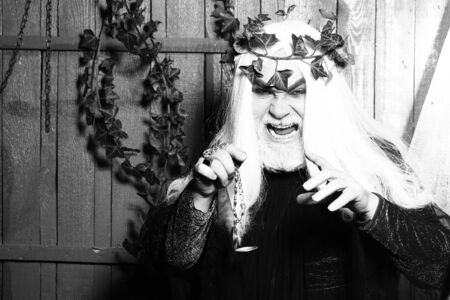Bearded senior sly strange man wizard in long white wig vine crown as Zeus god with medallion on...