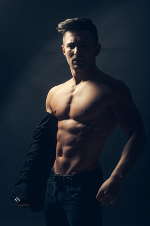 Handsome sensual sexy young stylish thoughtful man in black shirt with fashionable hairdo undressing with bare muscular torso and beautiful body indoor on studio background, vertical pictureの写真素材