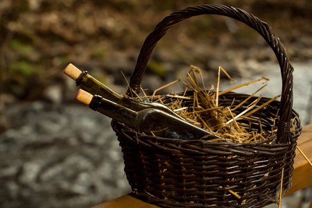 Wine bottles in picnic basket with straw near water in twilight. Vintage lookの写真素材