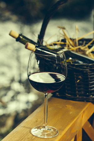 Wine glass and bottles in picnic basket with straw near water in twilight. Vintage lookの写真素材
