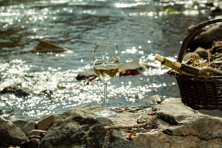 Wine glass and bottles in picnic basket with straw near water in twilight. Vintage lookの写真素材