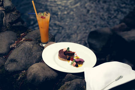 Picnic near water of orange juice and decorated dessert cake served with spoon on napkinの写真素材