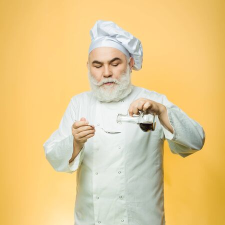 Bearded man cook in studio preparing food with sauce on yellow backgroundの写真素材