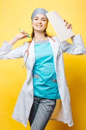 Confident young woman medical professional with stethoscope and papers isolated on yellow background. Medical person: Nurse / young doctor portrait.の写真素材