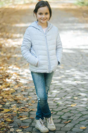 Beautiful girl with smiling face her hands in pockets posing in autumn park on natural backgroundの写真素材