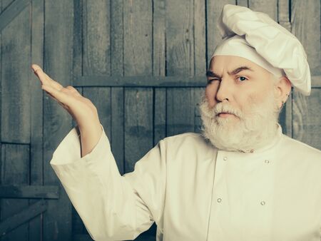 Bearded man cook in chef hat closeup in studio on wooden backgroundの写真素材