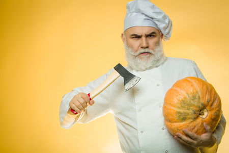 Bearded man cook in chef hat with axe and pumpkin on yellow backgroundの写真素材