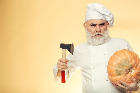 Bearded man cook in chef hat with axe and pumpkin on yellow backgroundの写真素材