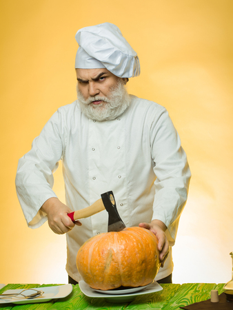 Bearded man cook in chef hat with axe and pumpkin on yellow backgroundの写真素材