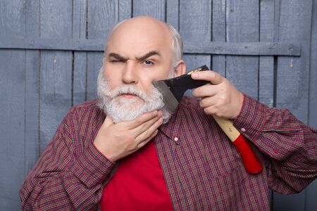 Senior man. Old man shaving white beard with axe on wooden background