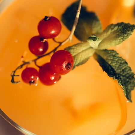 bright glasse with cold cocktail of orange juice decorated with viburnum and mint leaf closeup