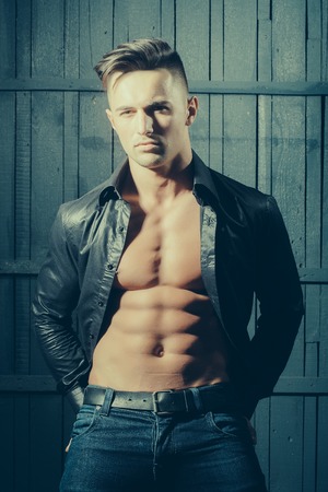 Handsome young sexy man with beautiful muscular chest in shirt in studio on wooden backgroundの写真素材