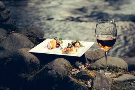Picnic near water, decorated fish meal with lemon, glass of wineの写真素材
