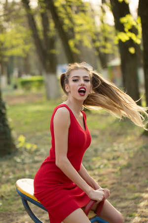 Young attractive girl on swing in red dress with funny hairstyle outdoorの写真素材