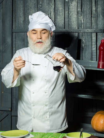 Bearded man cook in studio preparing food with sauce on wooden backgroundの写真素材