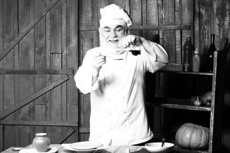 Bearded man cook in studio preparing food with sauce on wooden background, black and whiteの写真素材