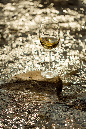 Wine glass with white wine standing on stone at seashore in sunset. Vintage lookの写真素材