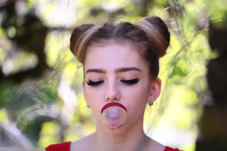 young pretty woman with chewing gum in the garden with fresh spring leaves on trees on blurred...