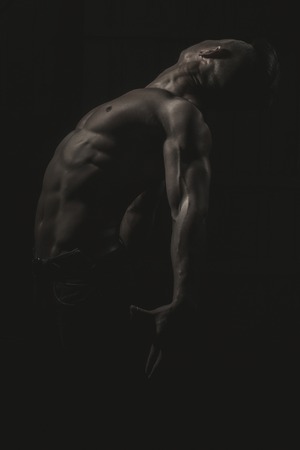 Muscular young man with athletic bare body standing on black backgroundの写真素材