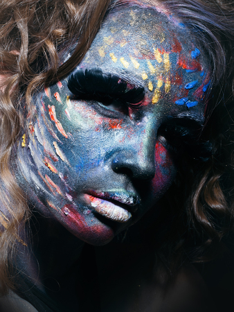 Woman with unusual paint make-up and curly hair in studioの写真素材