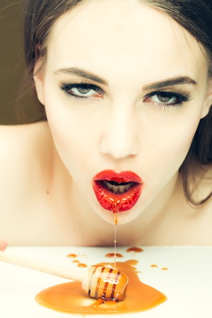 Sensual young woman with red lips eating honey from wooden spoonの写真素材
