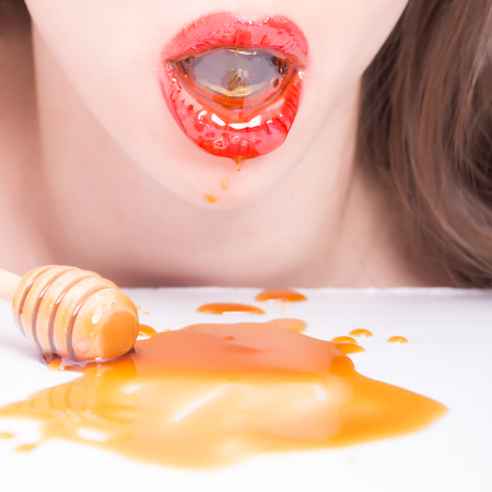 Sensual female red lips eating honey from wooden spoon closeupの写真素材