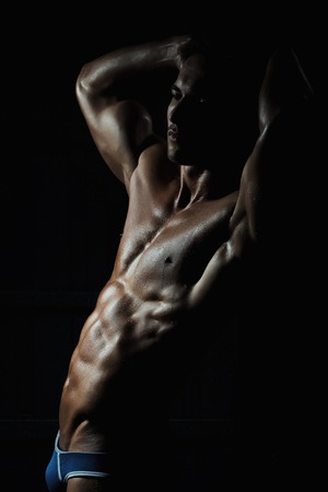 Muscular young man with athletic bare body standing on black backgroundの写真素材