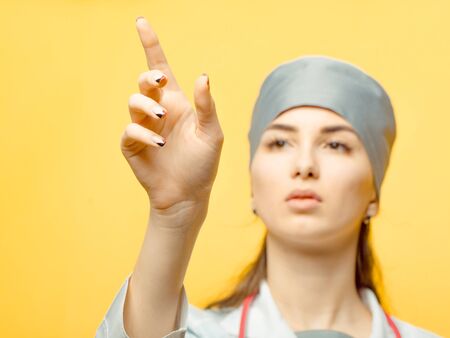 Young nurse with stethoscope showing with hand in medical hat in studio on yellow backgroundの写真素材
