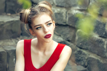 Beautiful sad young woman on a stone wall background posing with red lipsの写真素材