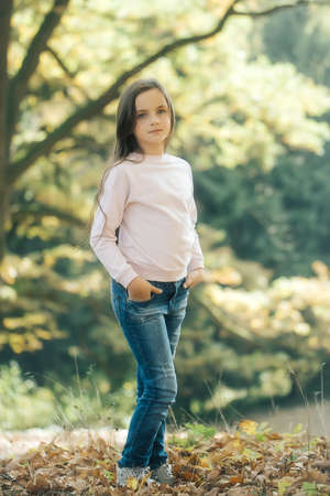Adorable girl adolescent brunette with serious face posing on tree foliage in autumn forestの写真素材